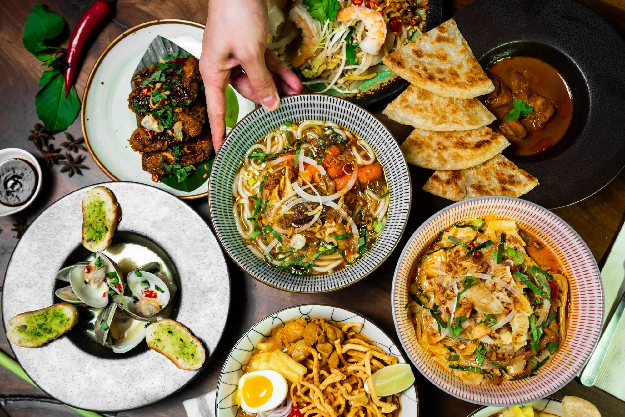 Overhead view of a shared table of noodle and rice dishes, dumplings and side plates.