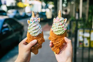 Two taiyaki cones filled with swirled soft serve, held up on the street.
